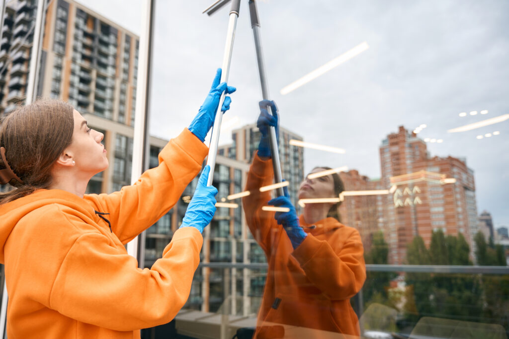 Young cleaning company worker washes windows with long-handled window mop