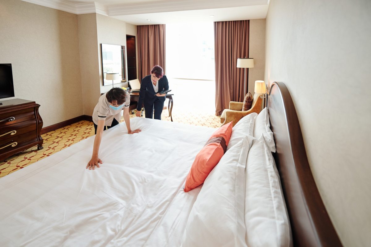 Hotel manager with digital tablet explaining new maid how to make bed properly
